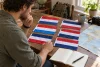 Un voyageur compare plusieurs petits drapeaux à bandes horizontales rouges, blanches et bleues.