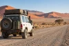 Un véhicule tout-terrain équipé roule sur une piste du désert namibien face aux dunes.